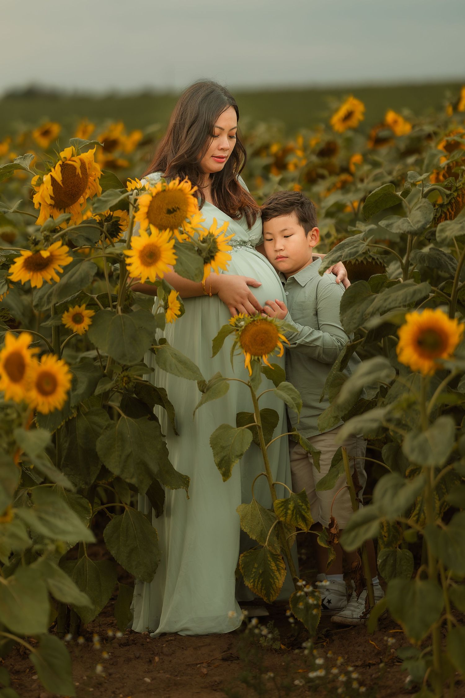 A person in a white dress stands thoughtfully among tall blooming sunflowers in a golden field at sunset.