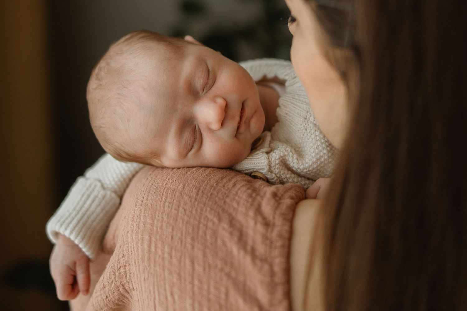 A baby wearing a peach-colored romper and white cardigan gently touches a soft blanket.