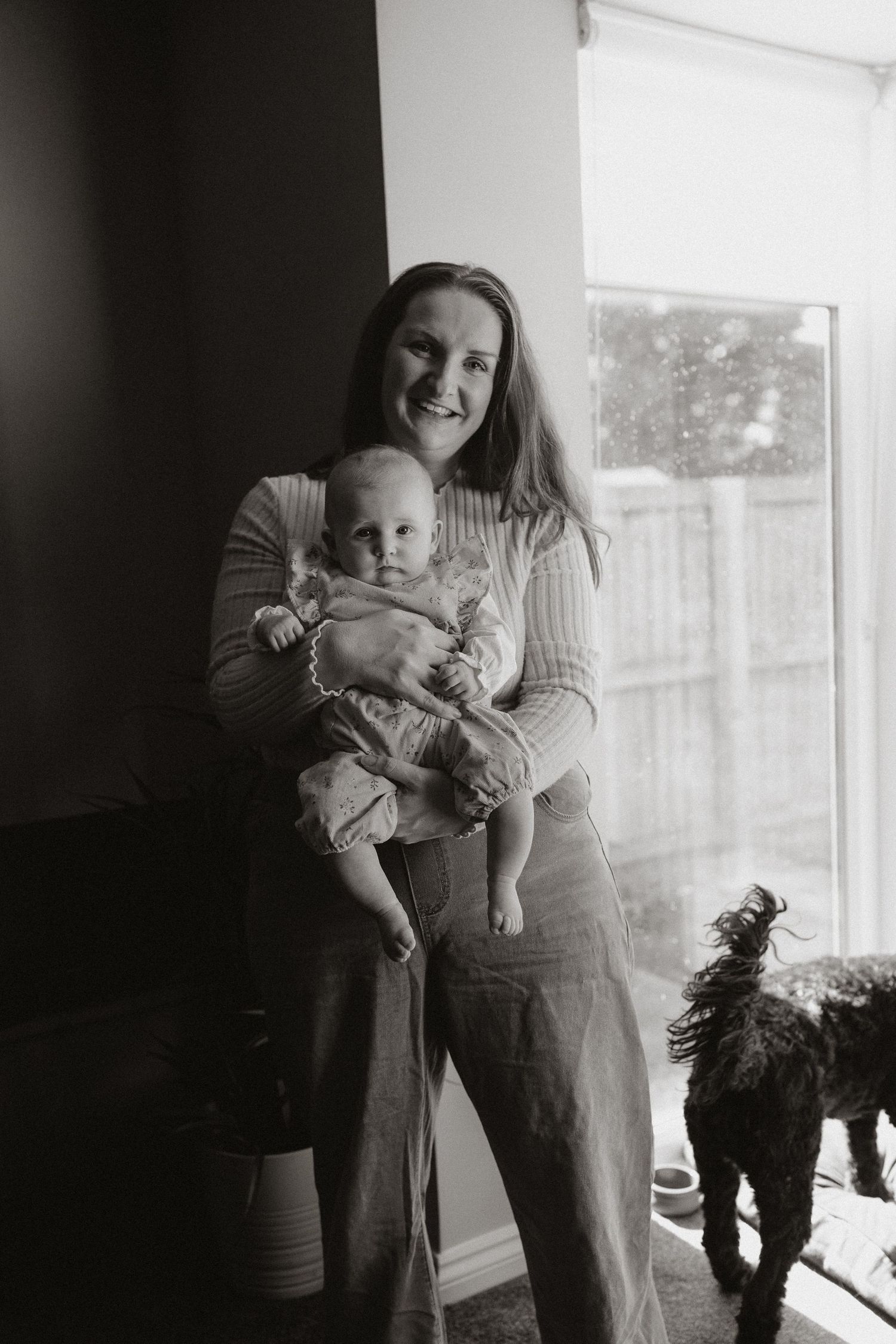 A series of black and white photos showing tender moments between a parent and baby near a window.