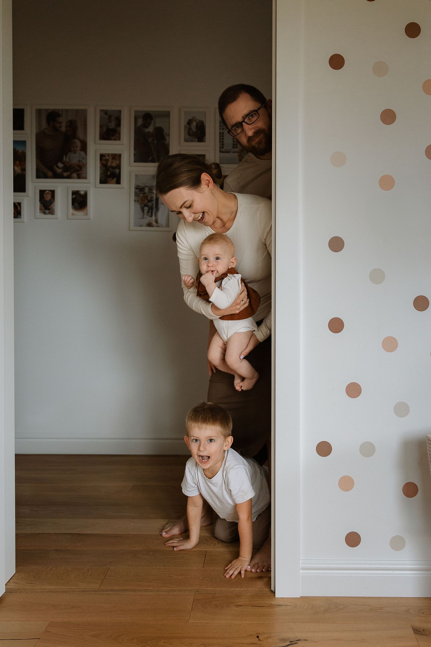 A playful series of photos showing a baby crawling and interacting with someone along a white wall with polka dot decor.