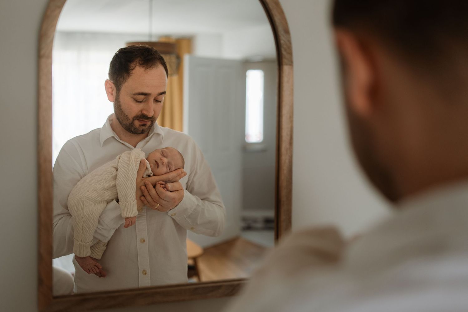 A person in a white shirt takes a bite of food while looking at themselves in a bathroom mirror.