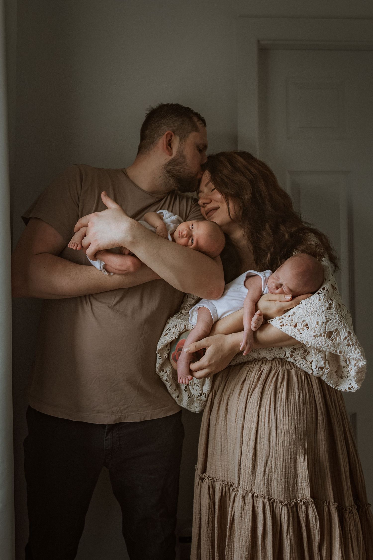 A tender family moment captured in a series of intimate black and white photographs showing parents embracing their newborn baby at home.