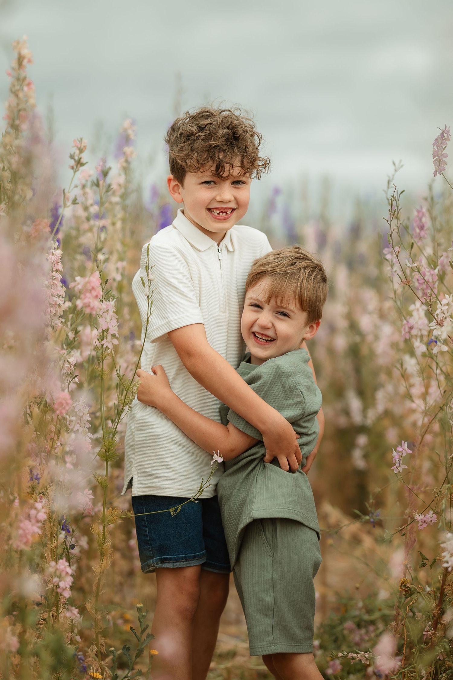 Two children playing and hugging in a field of purple wildflowers during a sunny outdoor photo session.