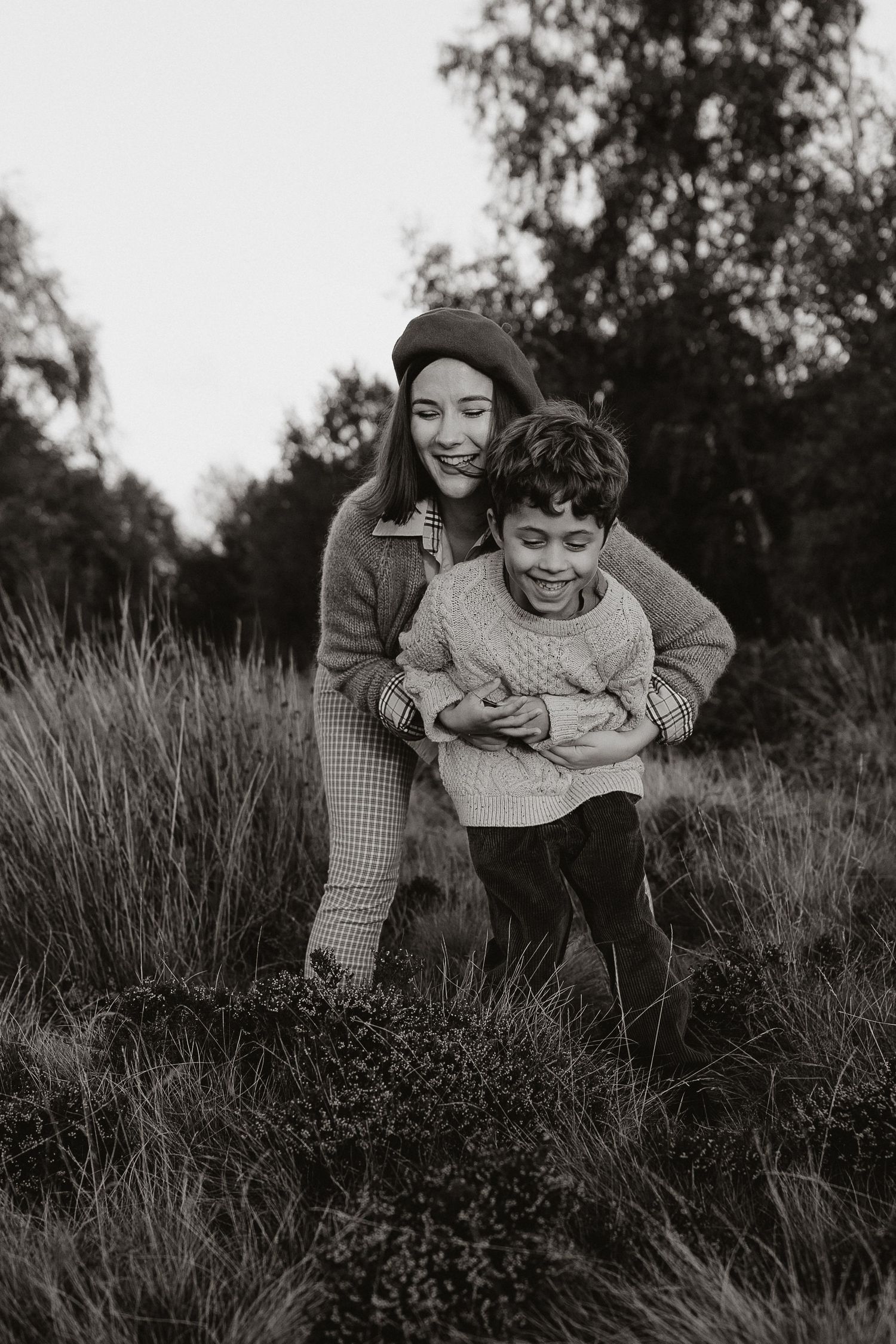 Black and white candid photos show playful moments between parent and child lying in tall grass outdoors.