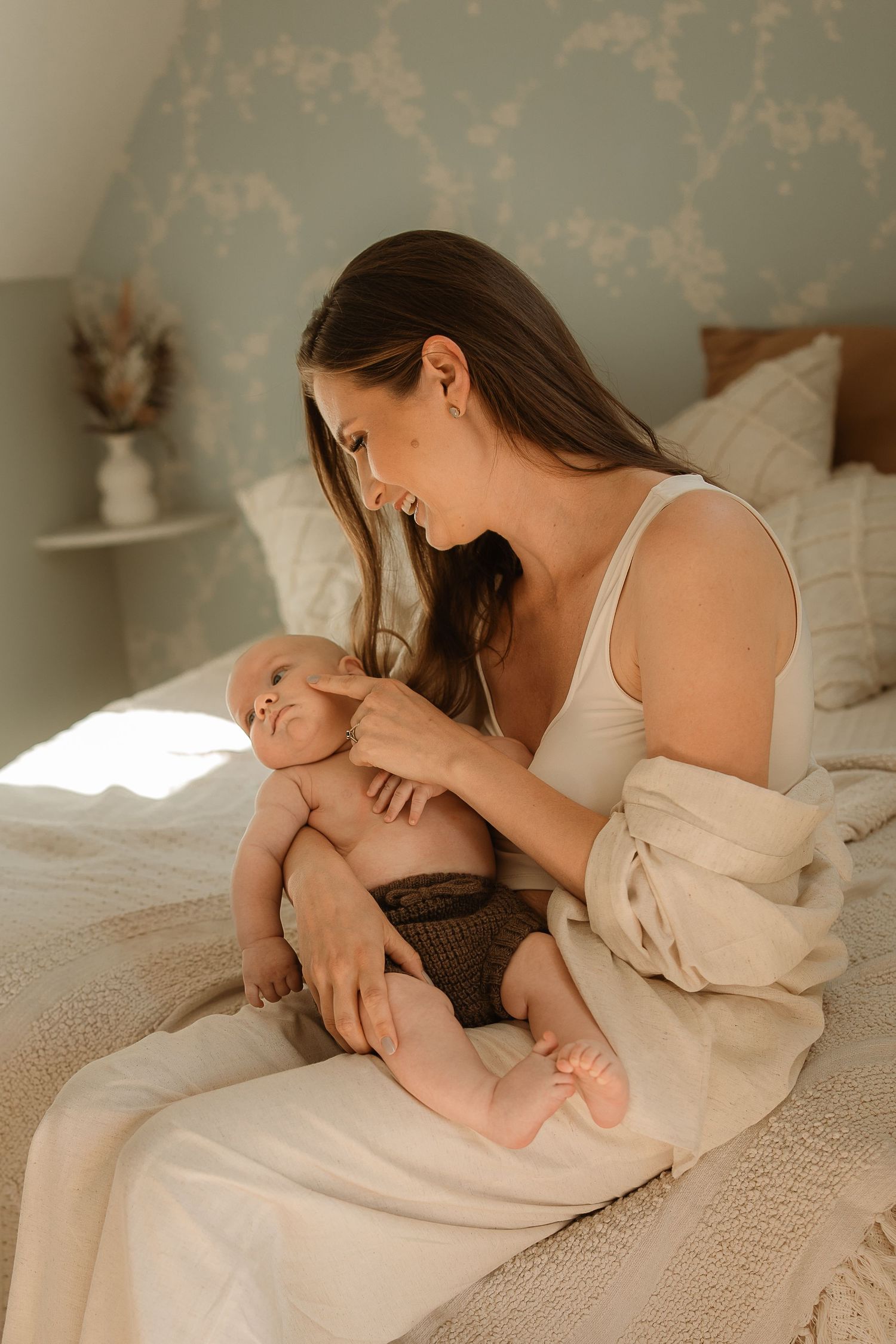 A tender moment between parent and baby lying on a textured white bedspread in soft natural lighting.
