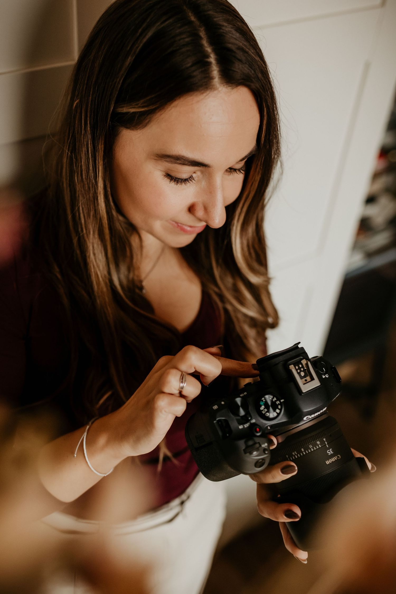 A photographer in a burgundy top examines a vintage film camera while taking photos in natural window light.