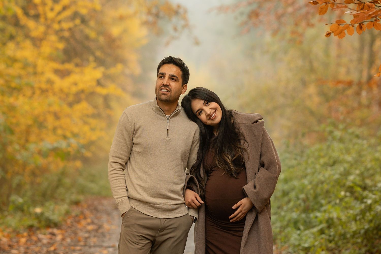 A couple embraces in an autumn forest setting with golden leaves and warm lighting creating a romantic atmosphere.