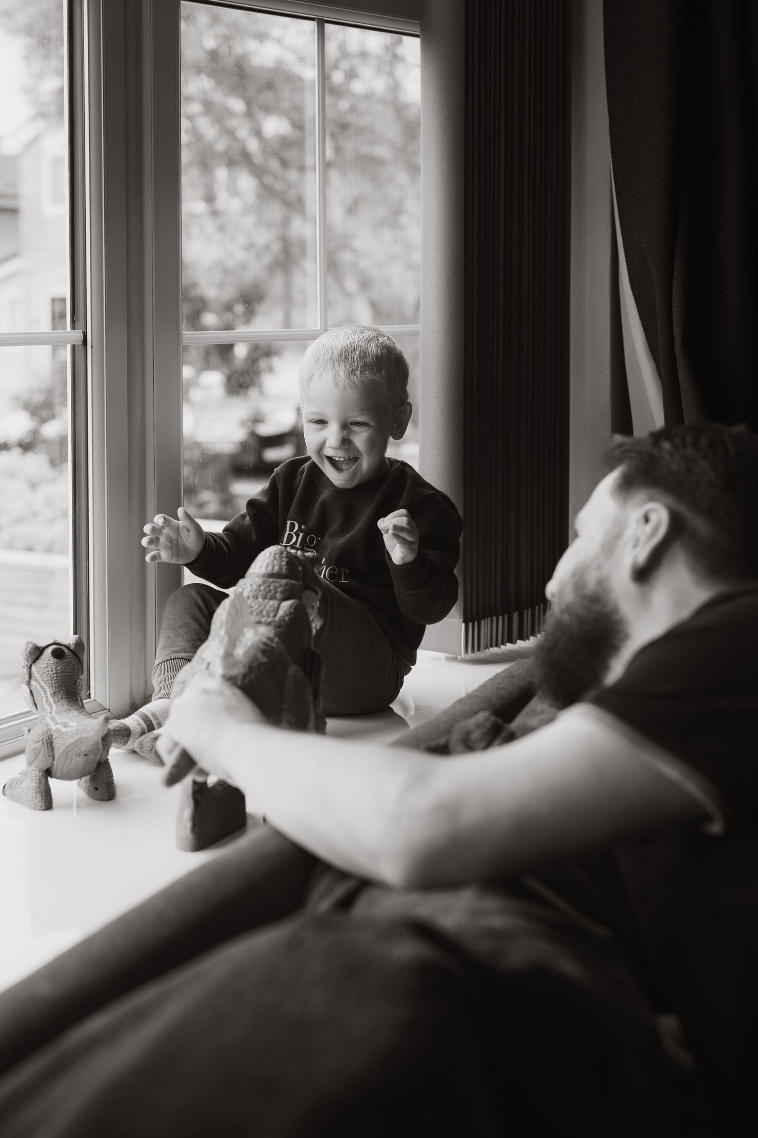 A series of candid black and white photographs showing joyful interaction between people by a window.