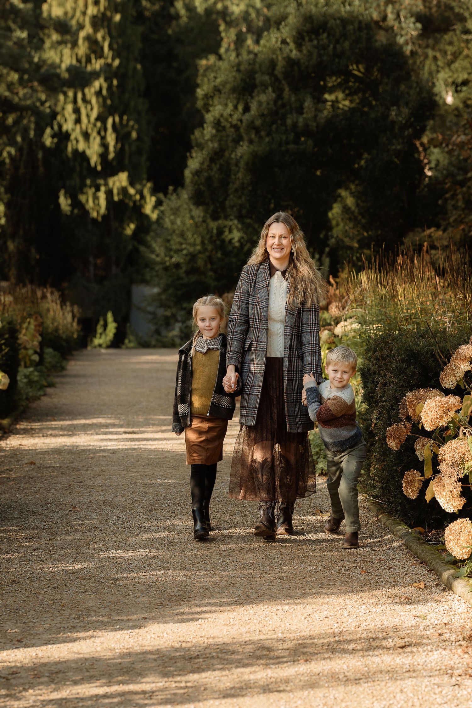 A family walks together on a gravel path lined with autumn hydrangeas and trees on a sunny afternoon.