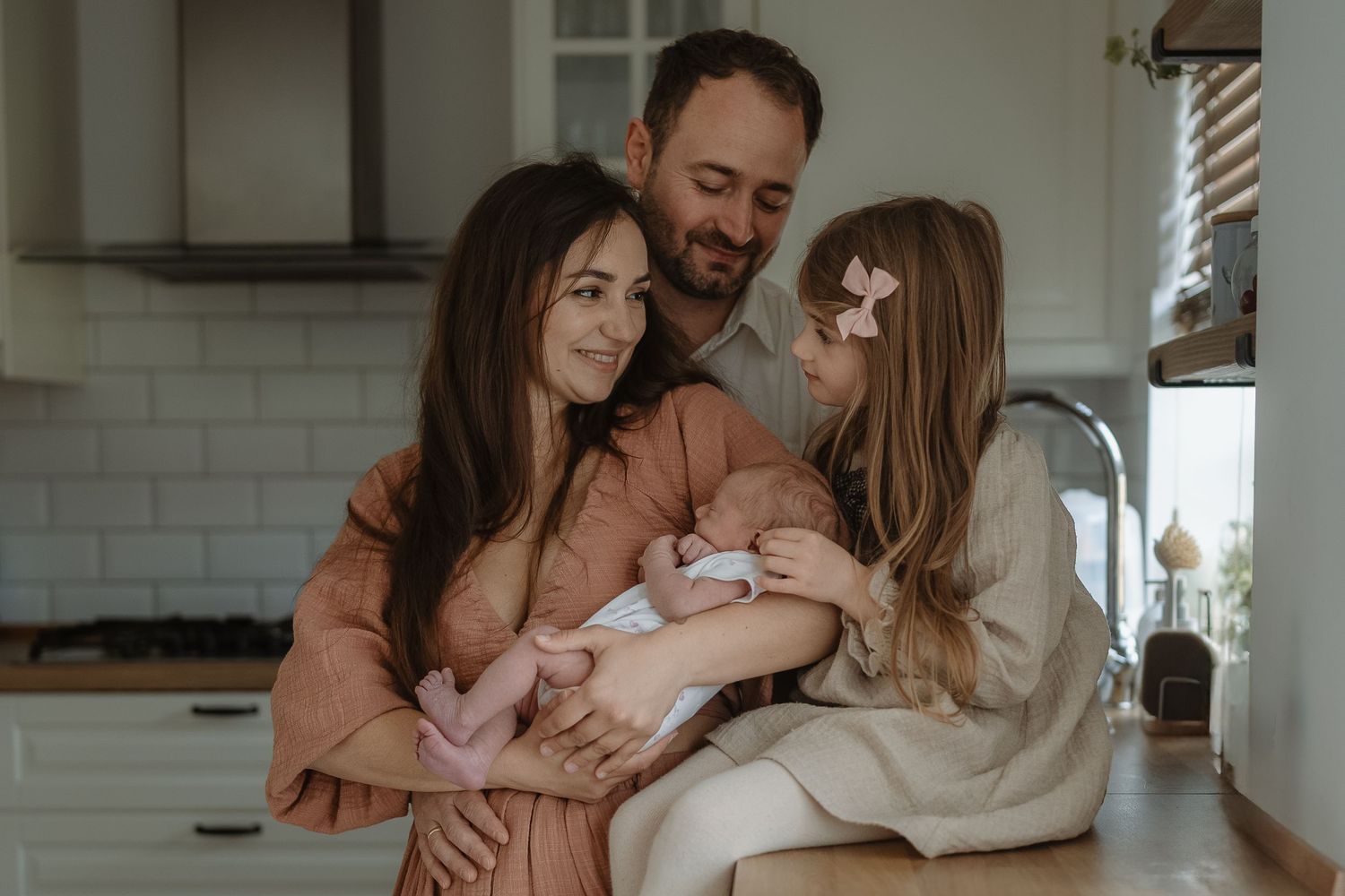 A loving family shares tender moments together in their bright white kitchen.