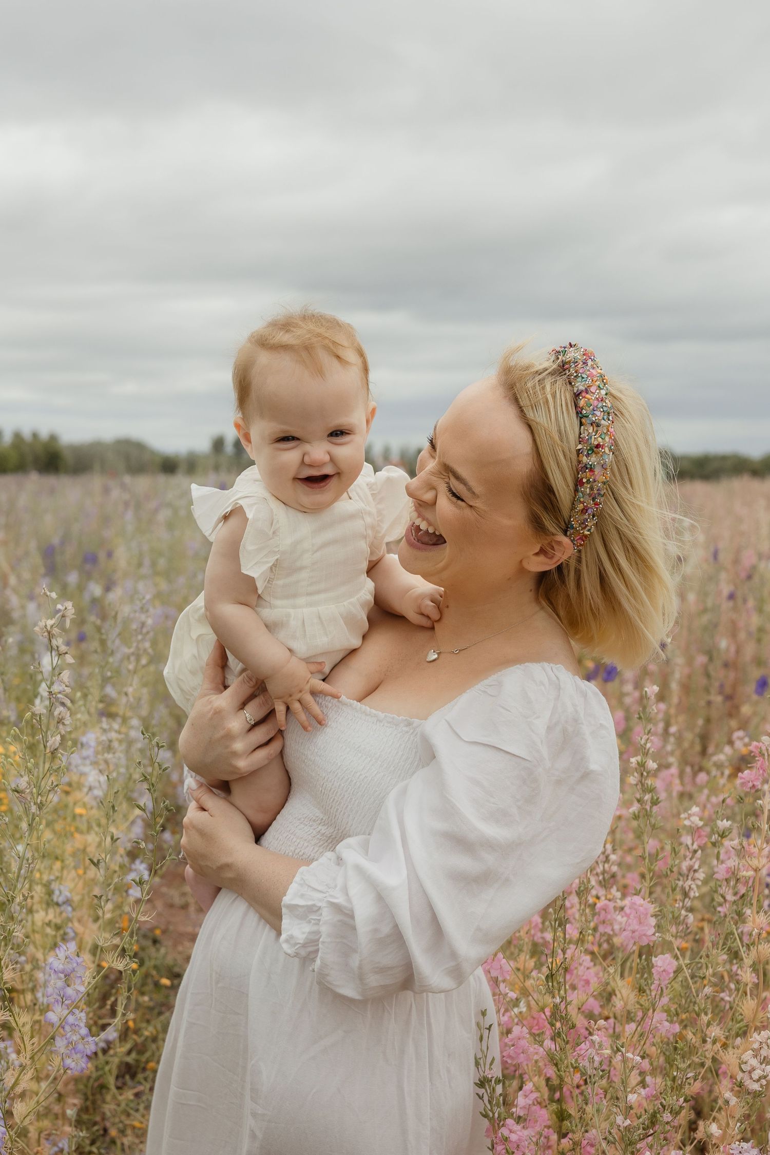 A joyful moment shared between mother and baby in a blooming wildflower field on an overcast day.