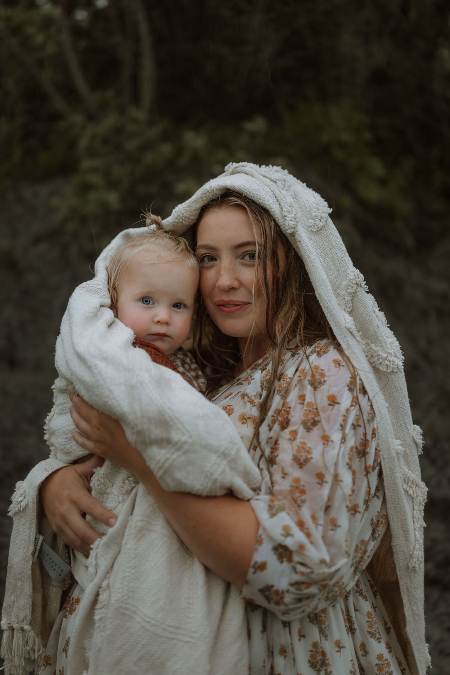 A mother and baby share tender moments in a series of intimate outdoor portraits wearing white and floral clothing.