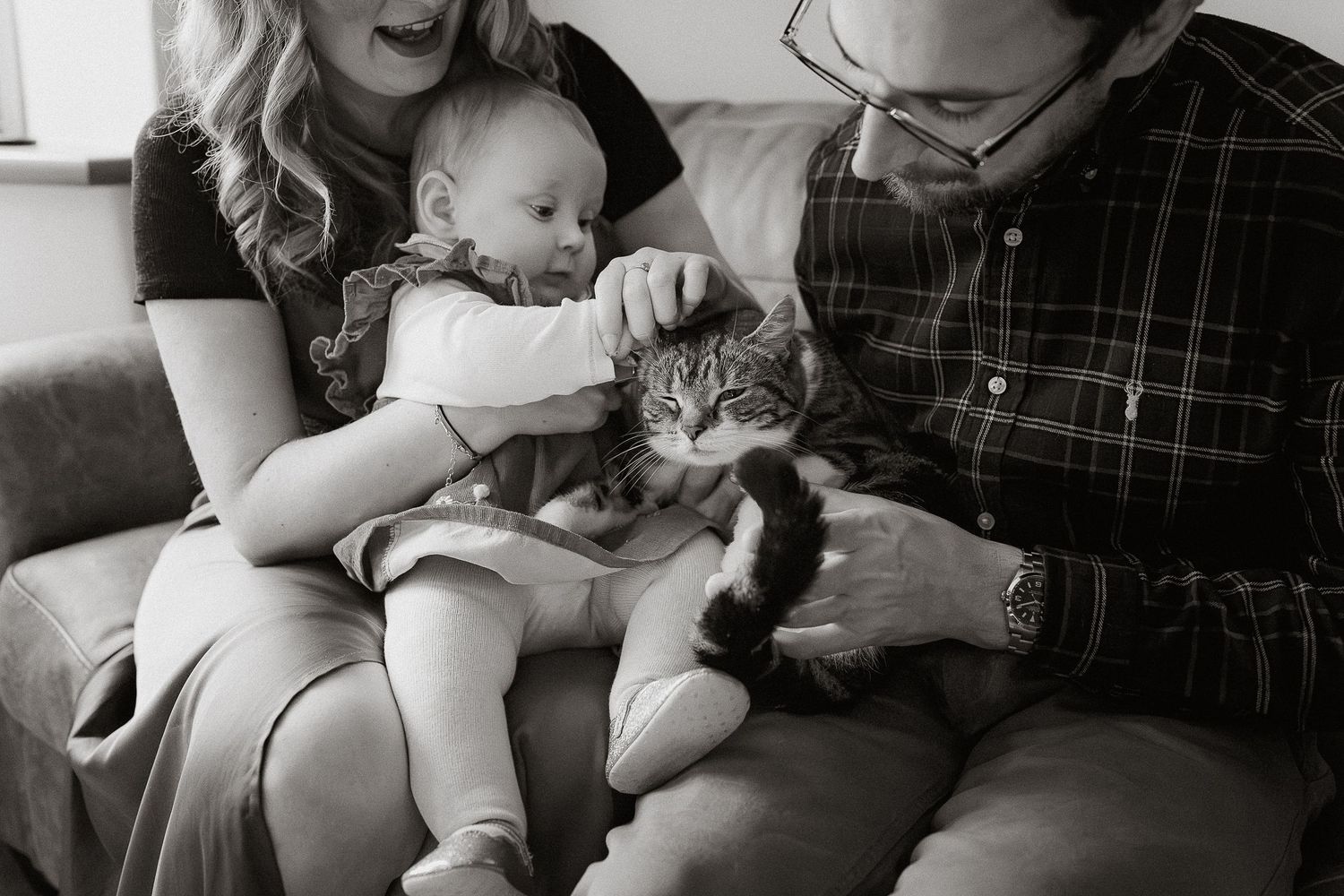 A series of black and white photos showing tender moments between a baby and a cat sitting together.