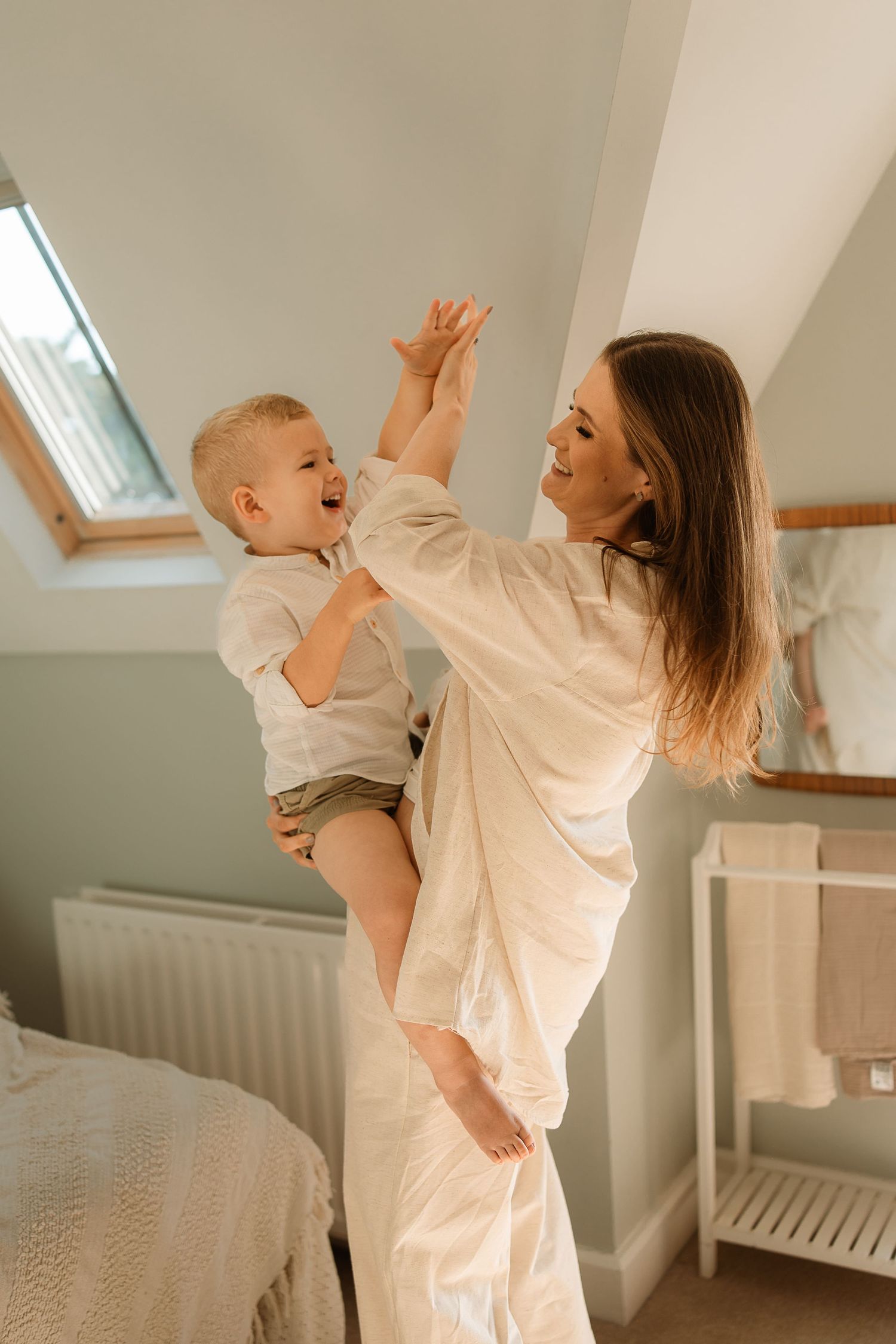 A parent and baby in matching white outfits dance together playfully in a bright, airy room.