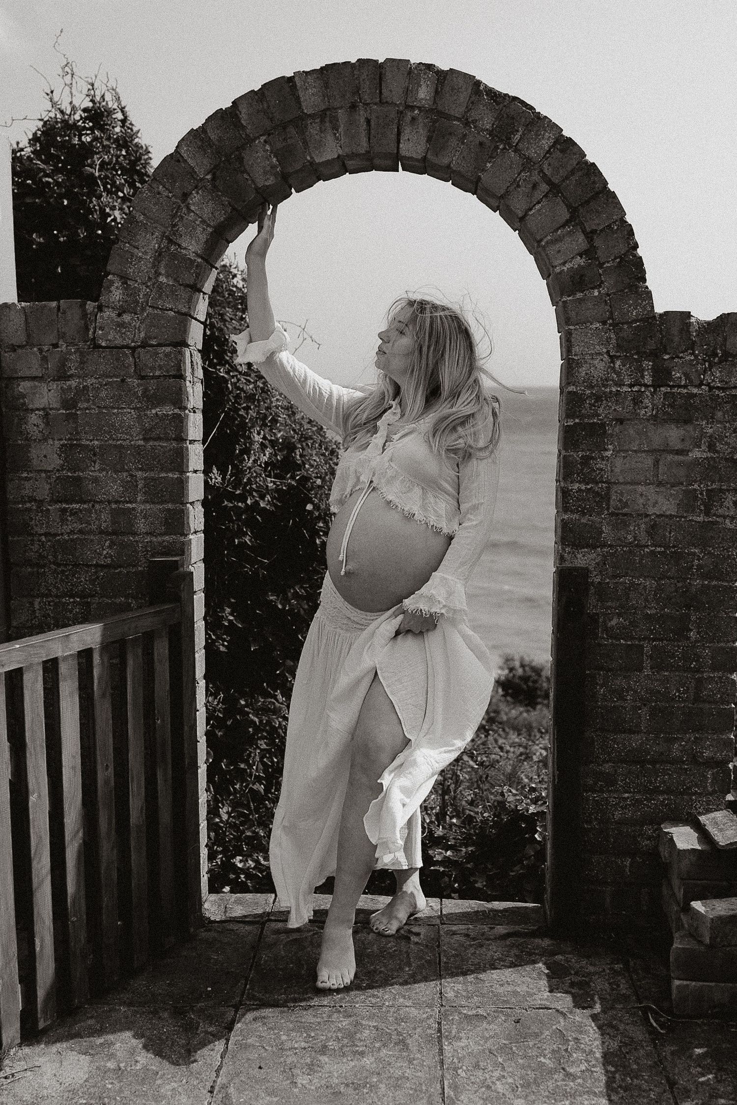 A series of black and white photos showing a figure in white clothing moving through a stone archway in different poses.