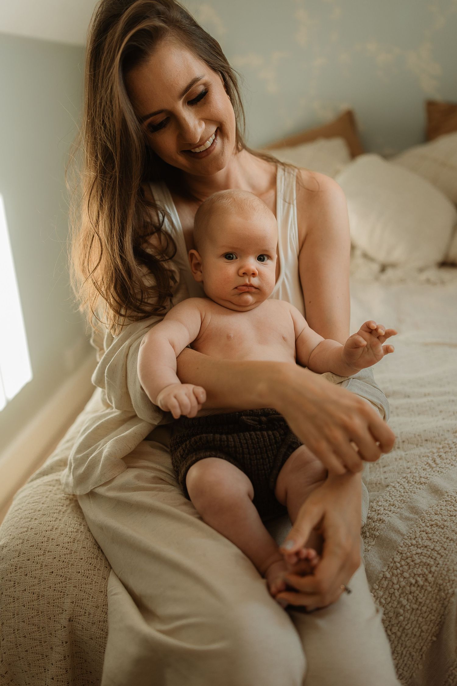 A tender moment captured as a mother and baby share loving interactions while sitting together on a cozy bed.