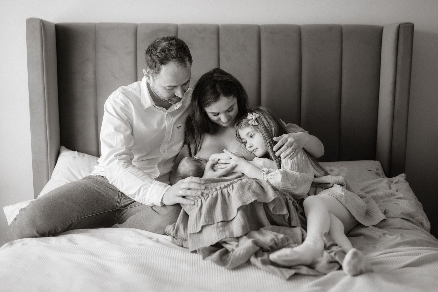 A series of black and white photos show tender family moments in bed with parents and children reading together.