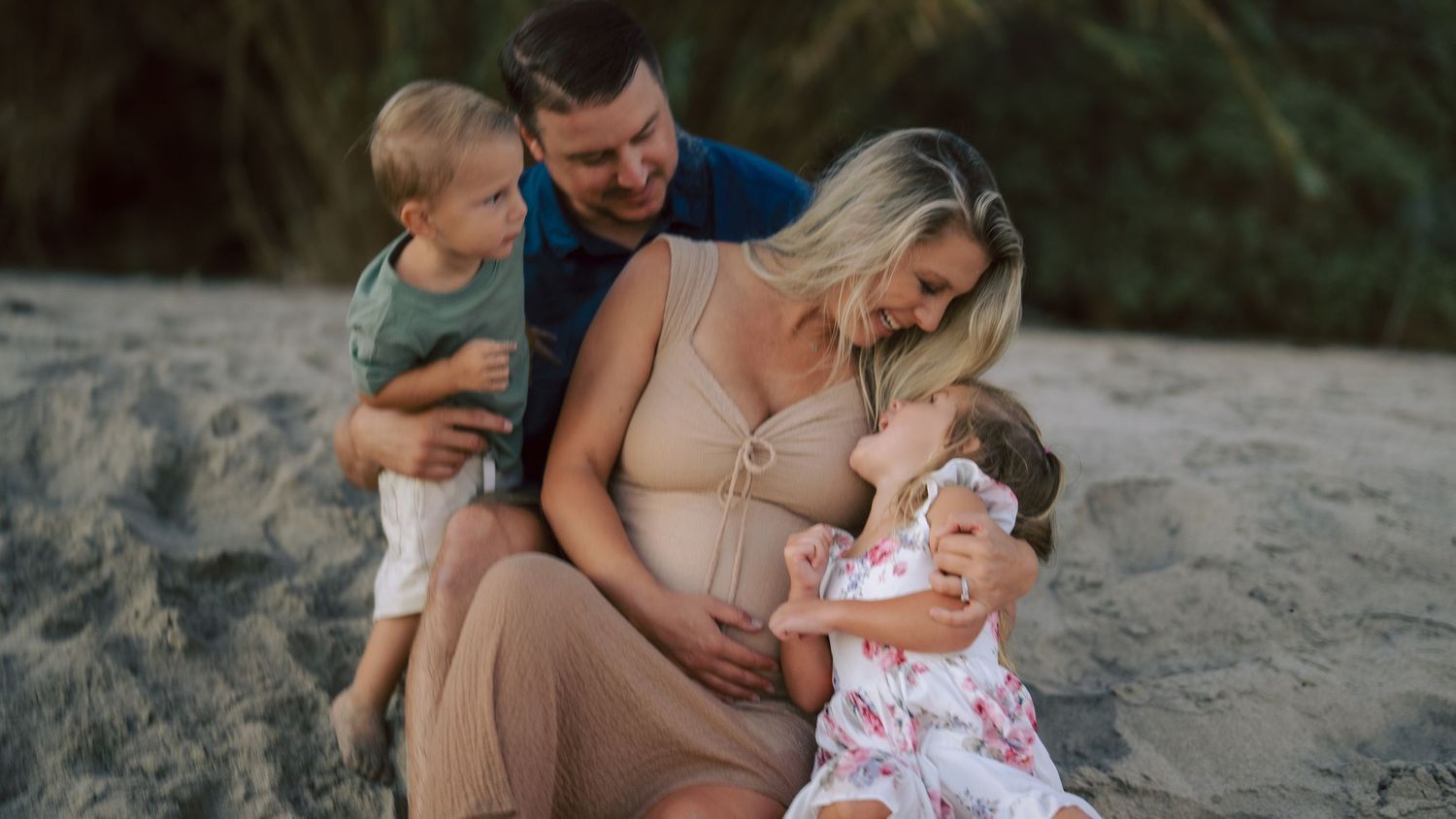 Happy pregnant mother with husband and two children cuddling together on sandy beach.