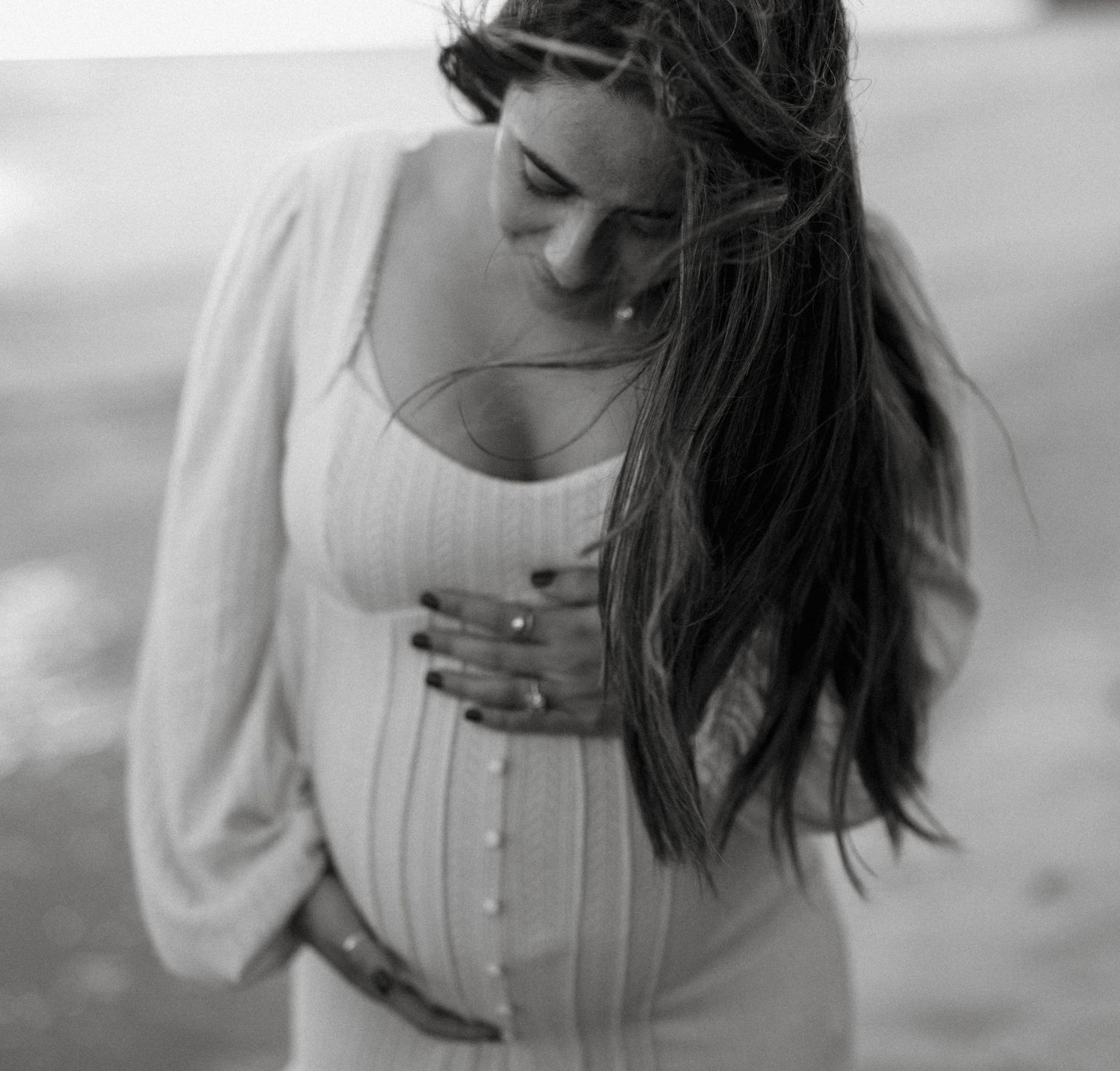 Black and white portrait of pregnant woman looking down, hand on belly.