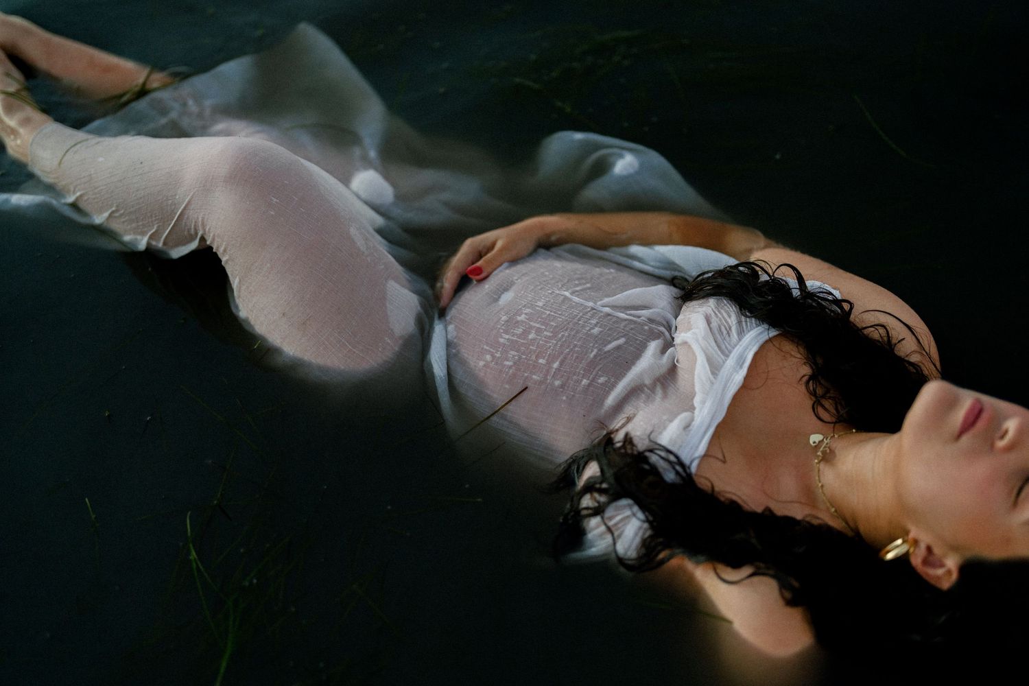 Ethereal underwater maternity photo of pregnant woman in white dress floating gracefully.