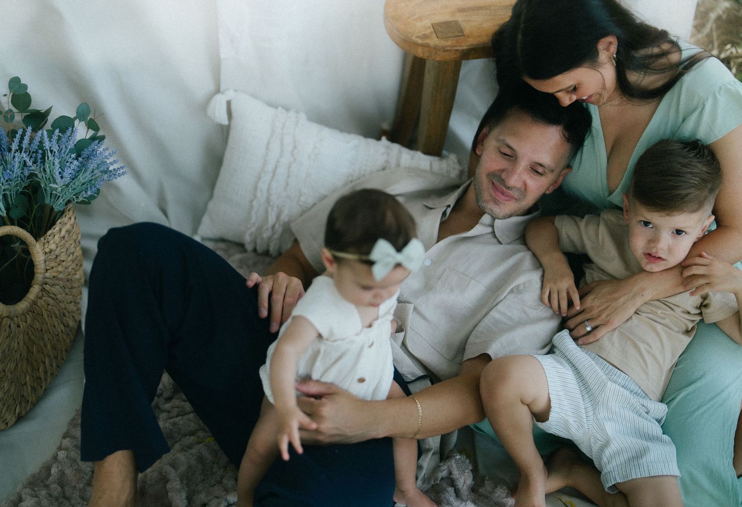Happy family with two toddlers relaxing together on a cozy floor setup in a bright, airy home setting.