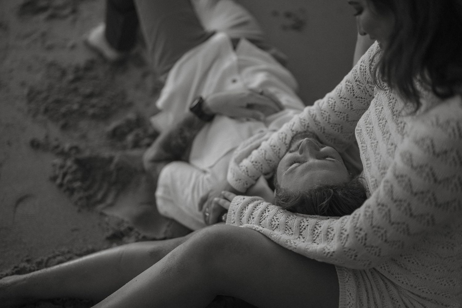 Tender black and white beach photo of couple relaxing together on sandy shore.