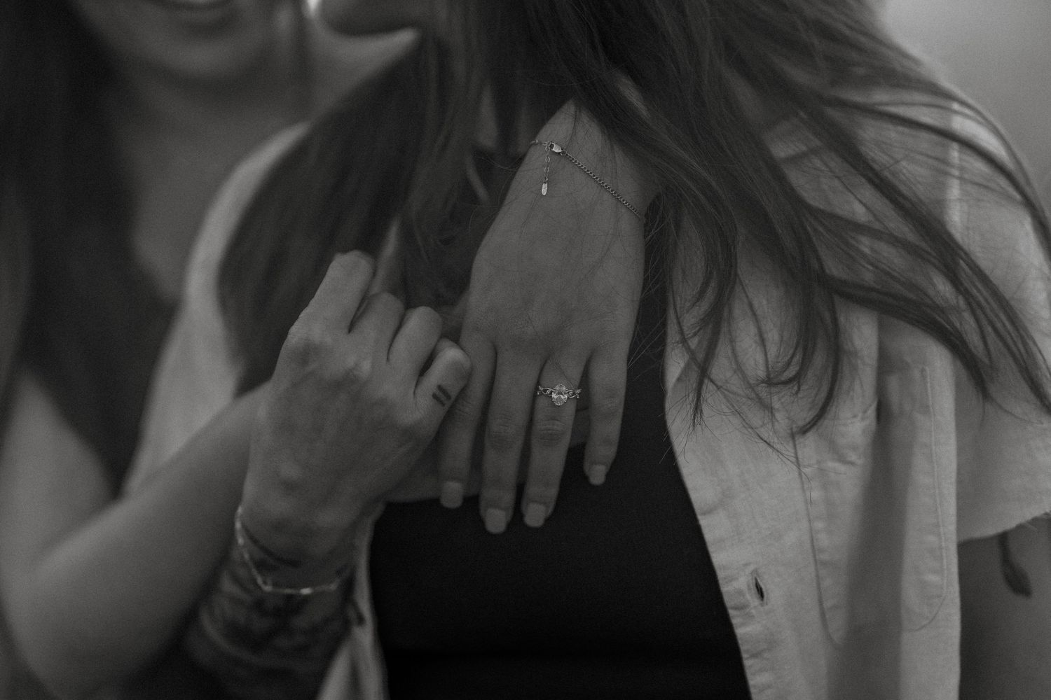 Close-up black and white photo of hands showing an engagement ring on a womans finger.