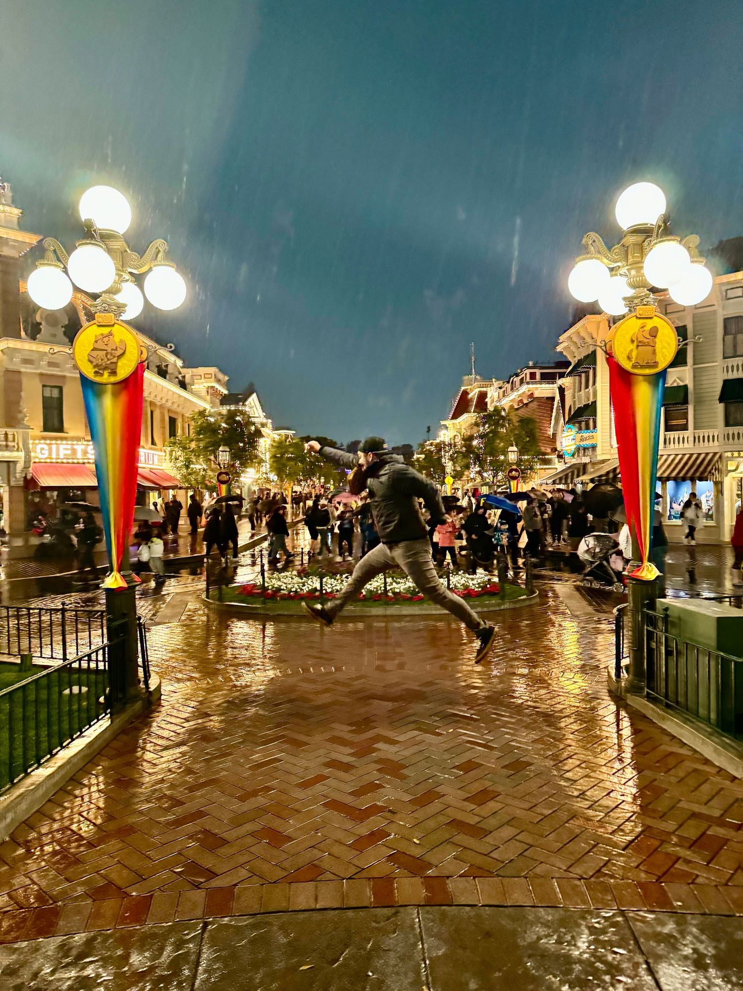 Person jumping joyfully on wet Main Street at Disneyland during rainy evening.