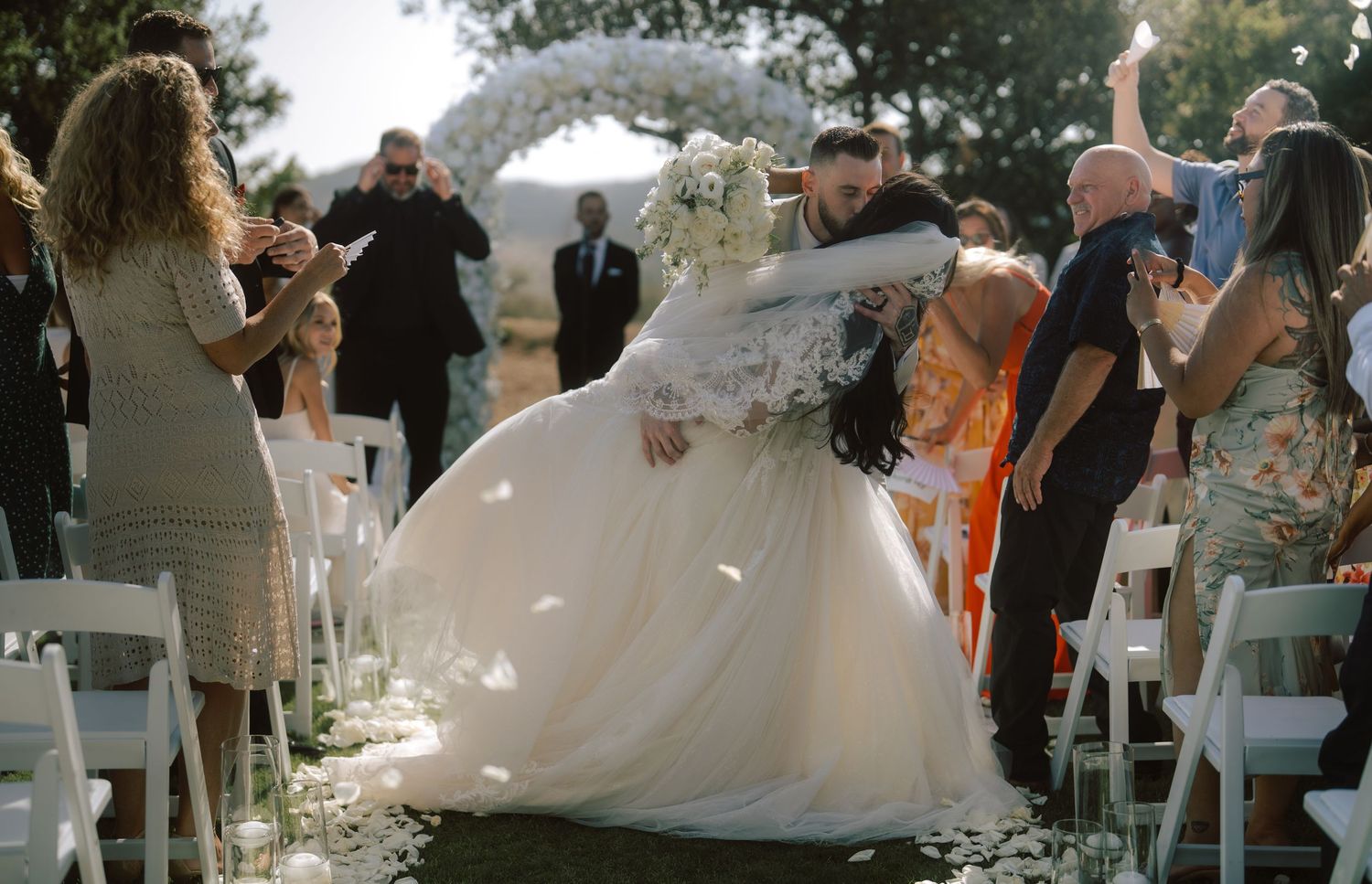 Groom lifts bride joyfully as guests celebrate along the wedding ceremony aisle.