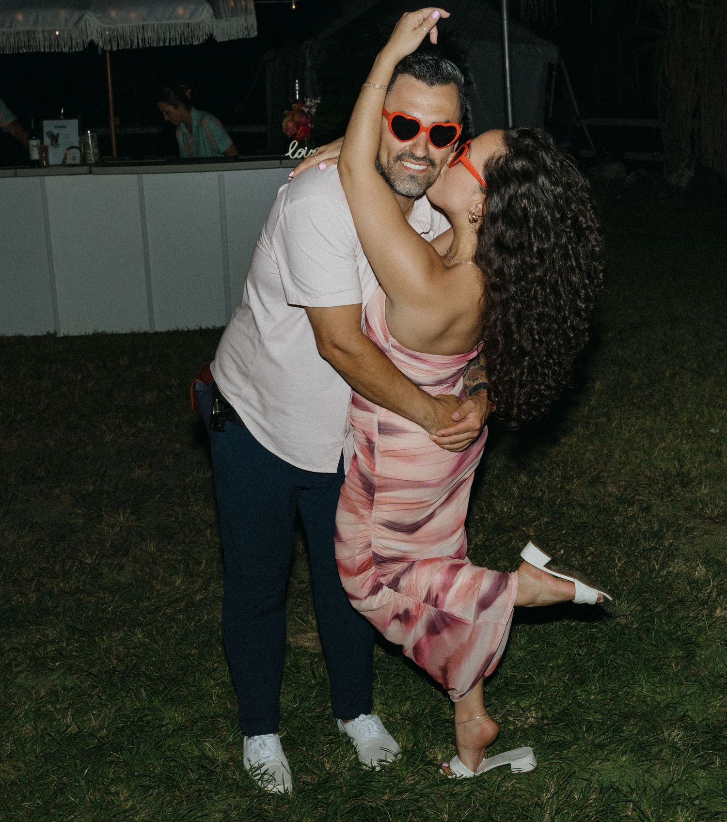 Couple dancing outdoors at night wearing red heart sunglasses at a casual outdoor party event.