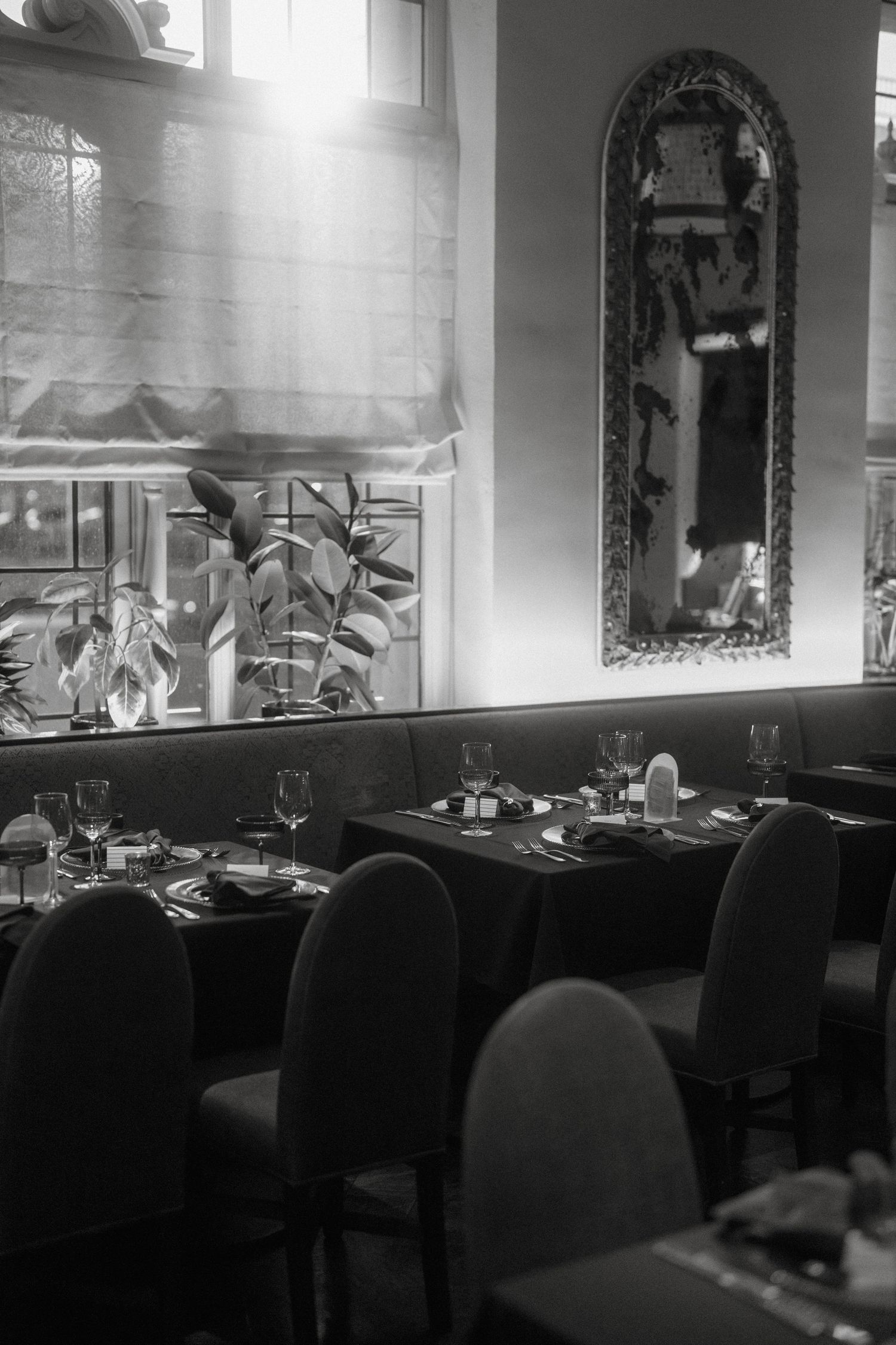 Black and white photo of elegant restaurant interior with set tables and mirror.