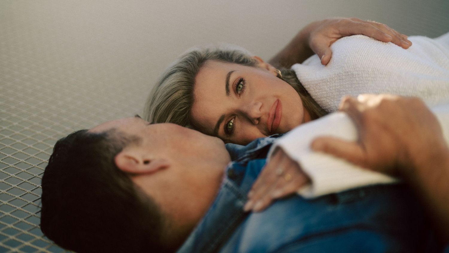 Woman resting her head on her partners chest while lying on a grid surface during an intimate couples shoot.