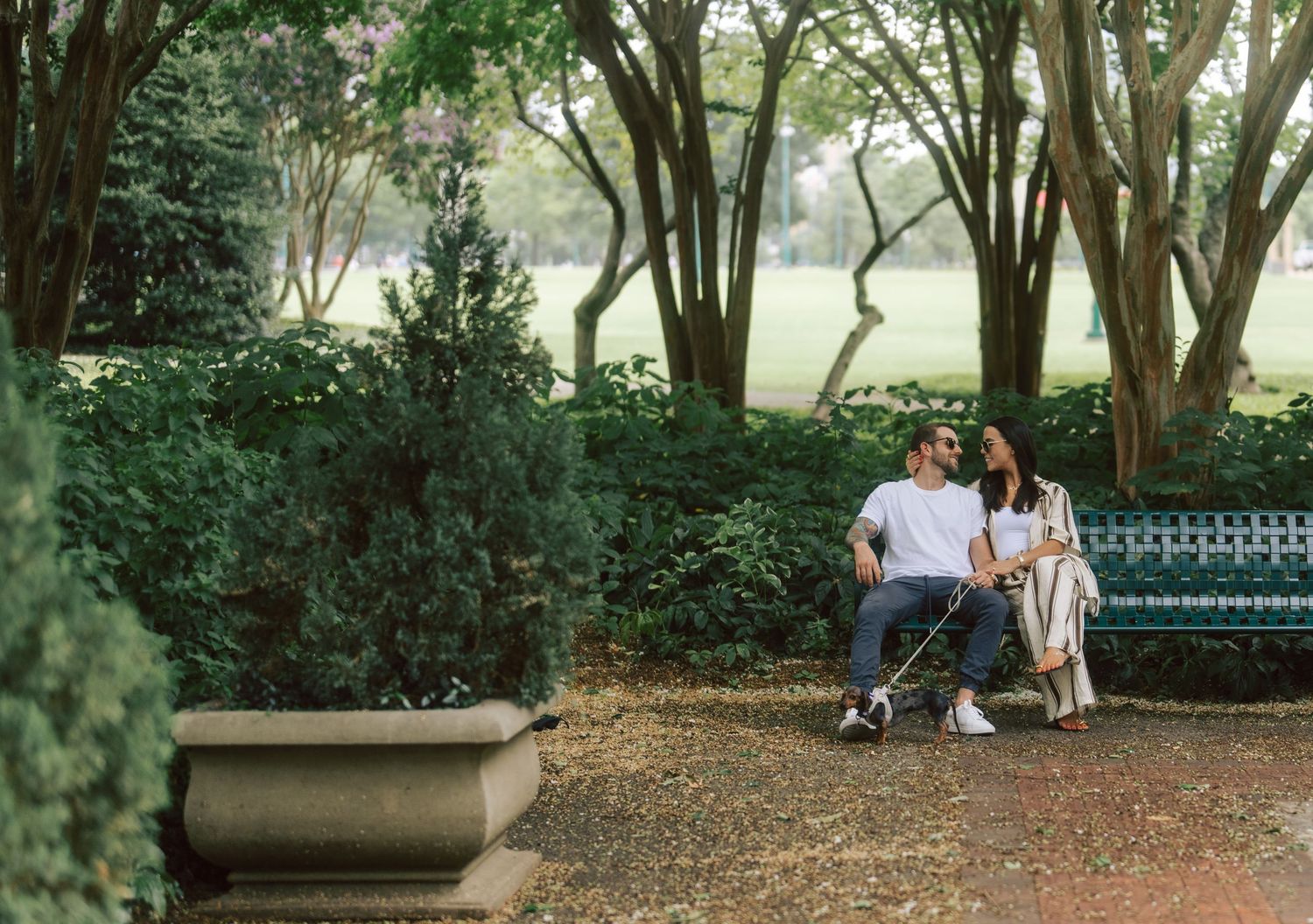 Couple sitting together on a bench in a serene garden setting with green shrubs and trees.