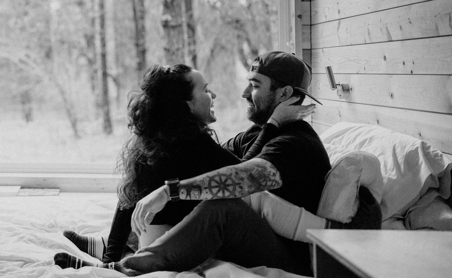 Couple sharing intimate moment together sitting on bed near window in black and white photo.
