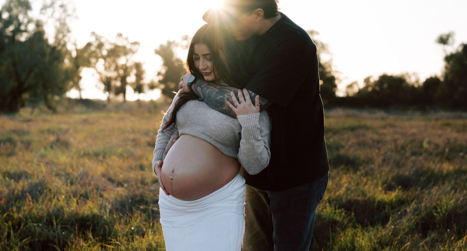 Couple sharing a tender maternity moment in a sunlit golden field at sunset.