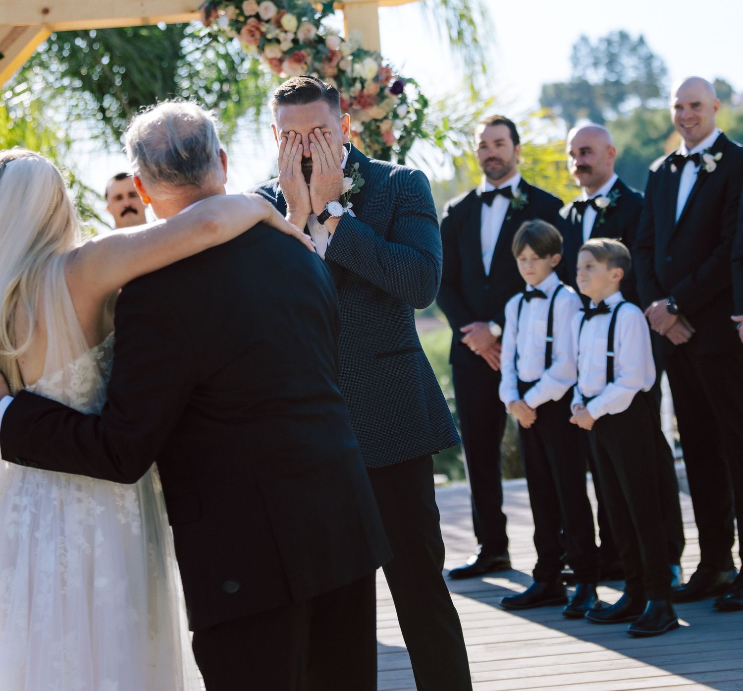 Emotional groom covering his face as he sees his bride walking down the aisle at outdoor wedding.