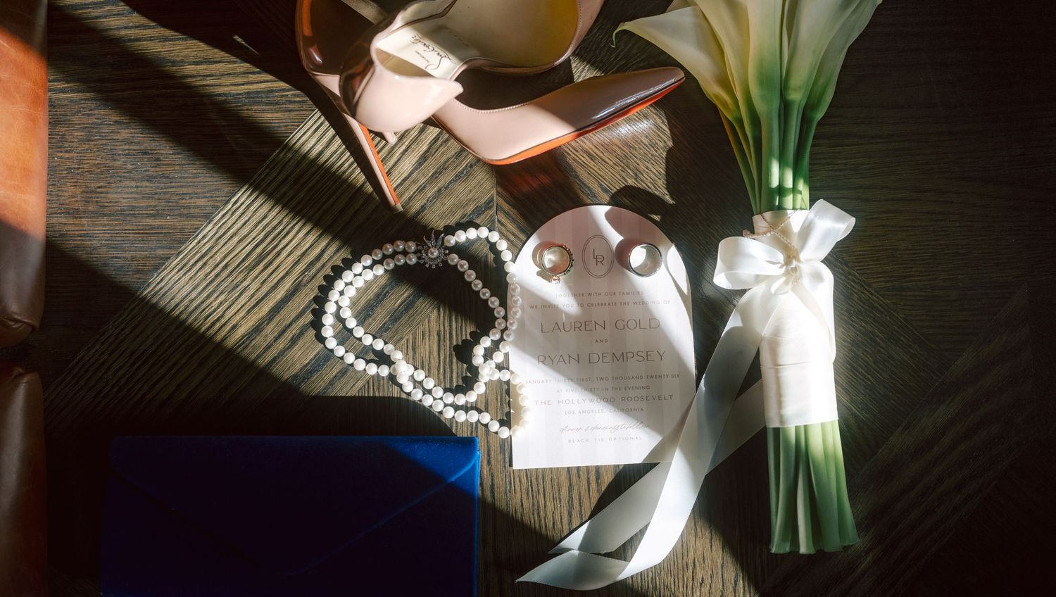 Wedding flat lay with pearl bracelet, bouquet, heels, and accessories on wood.