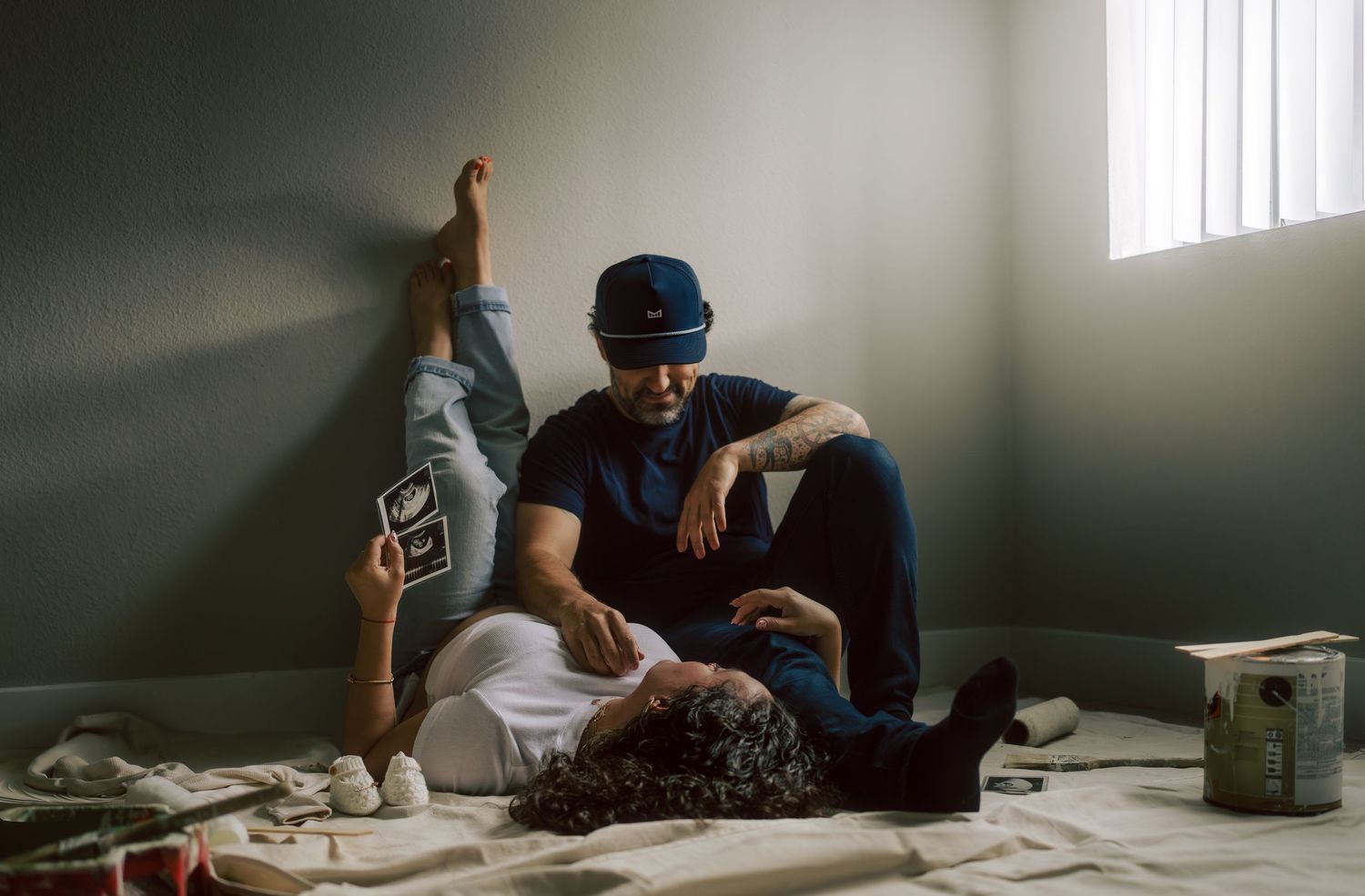 Man sitting on floor cradling partner holding ultrasound in freshly painted room.
