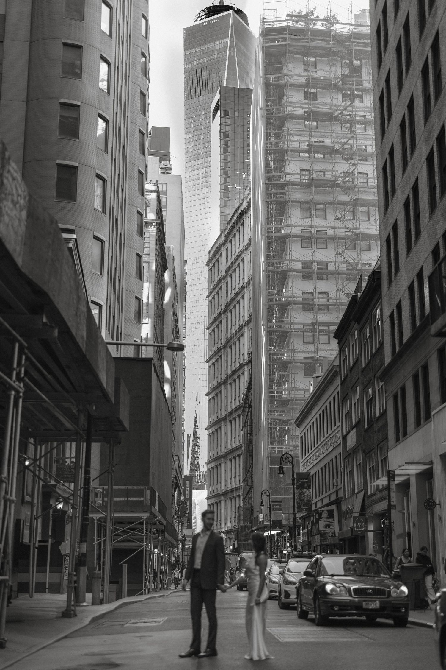 Black and white photo of bride and groom standing in a Manhattan street with One World Trade Center towering above.