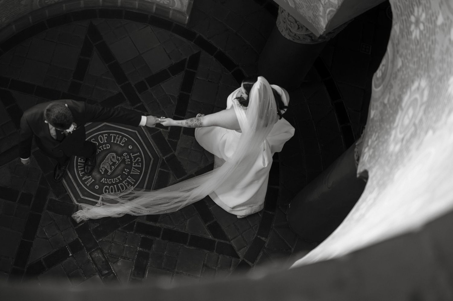 Aerial black and white wedding photo of bride and groom dancing on ornate floor.
