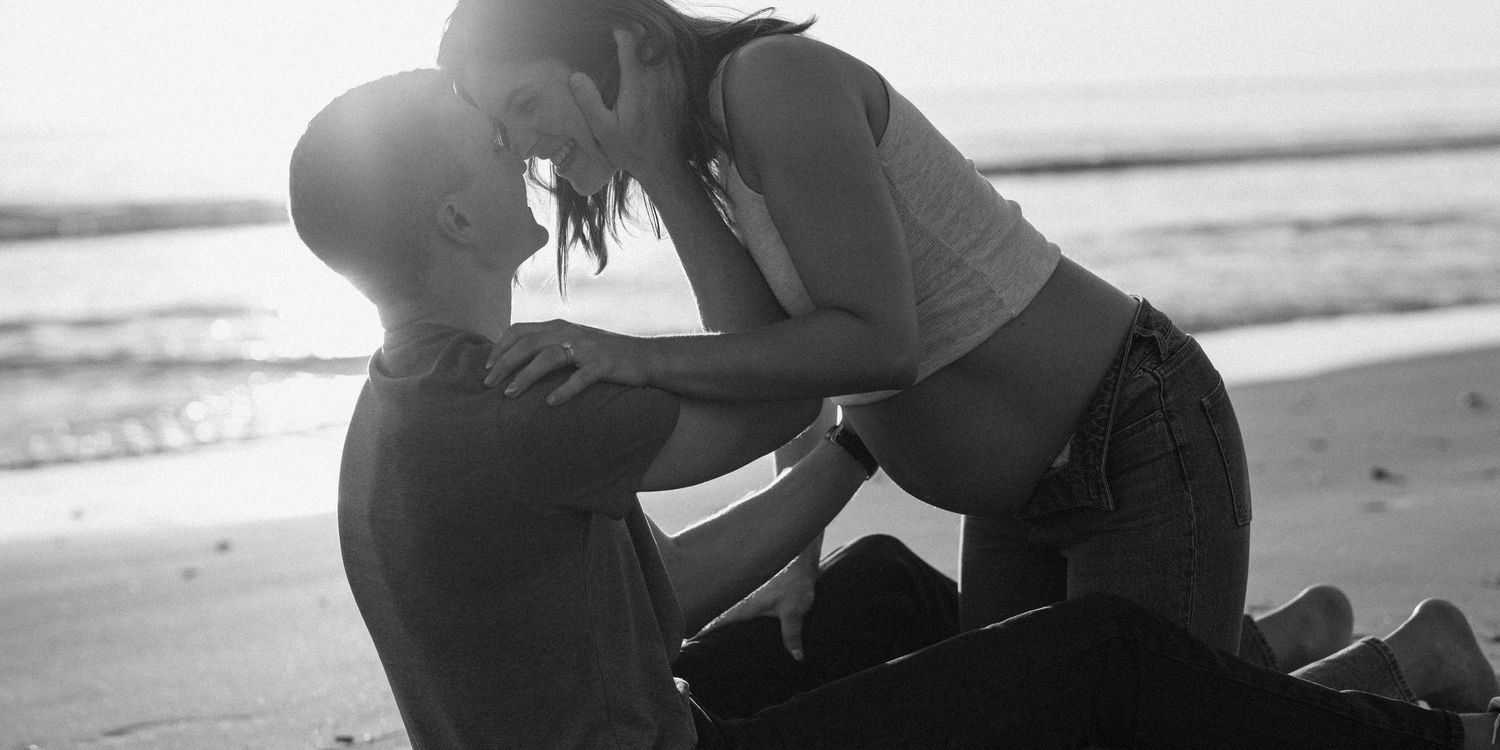 Black and white romantic beach photo of couple embracing at sunset.