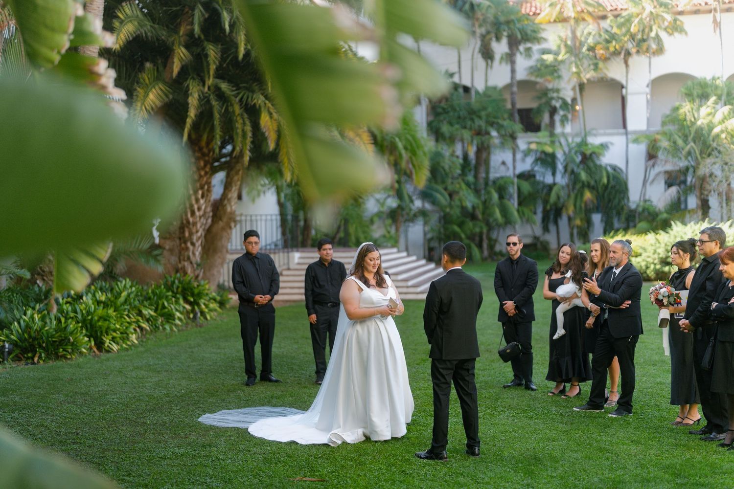 Intimate outdoor wedding ceremony on green lawn with bride and groom exchanging vows among small guest group.