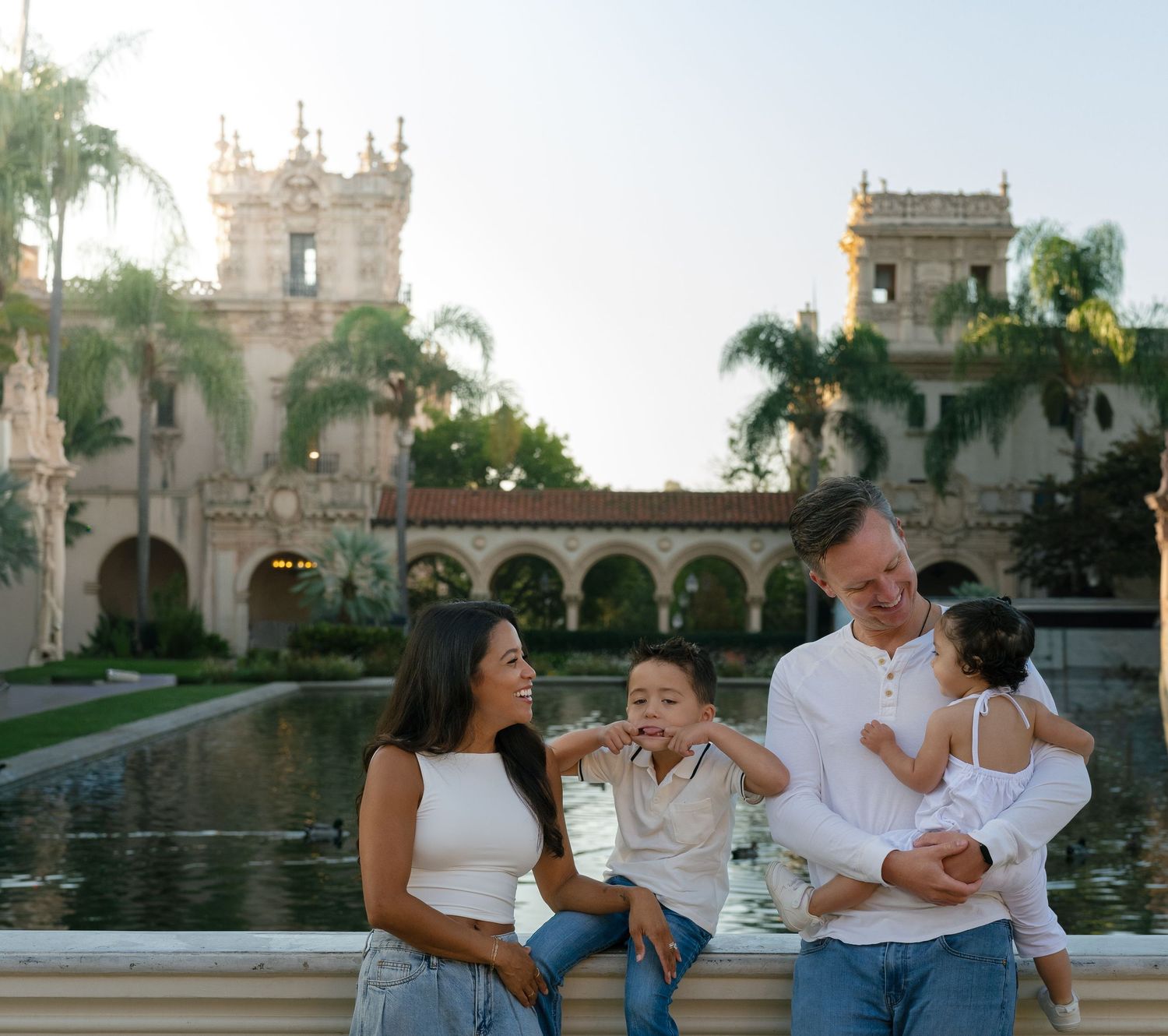 Happy family of four posing near a reflecting pool with historic building backdrop.