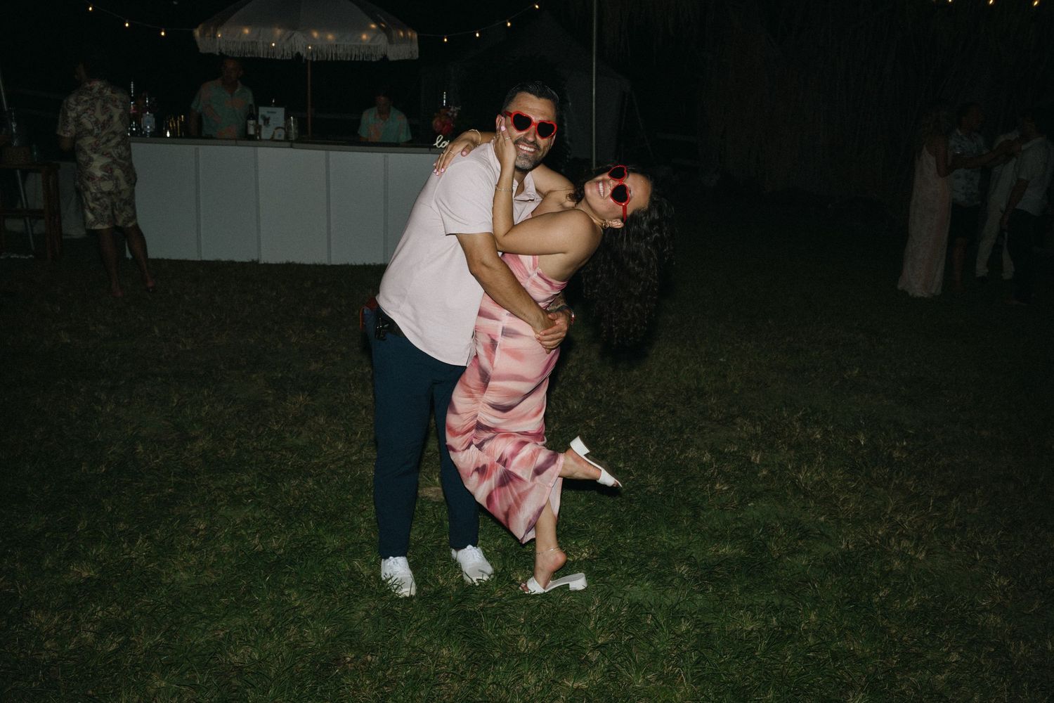 Couple dancing and laughing outdoors at night during wedding reception.