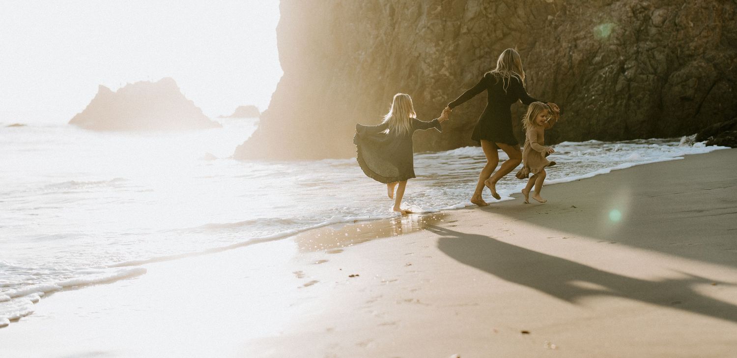 Family joyfully along a sunlit beach with dramatic rock formations in the background.