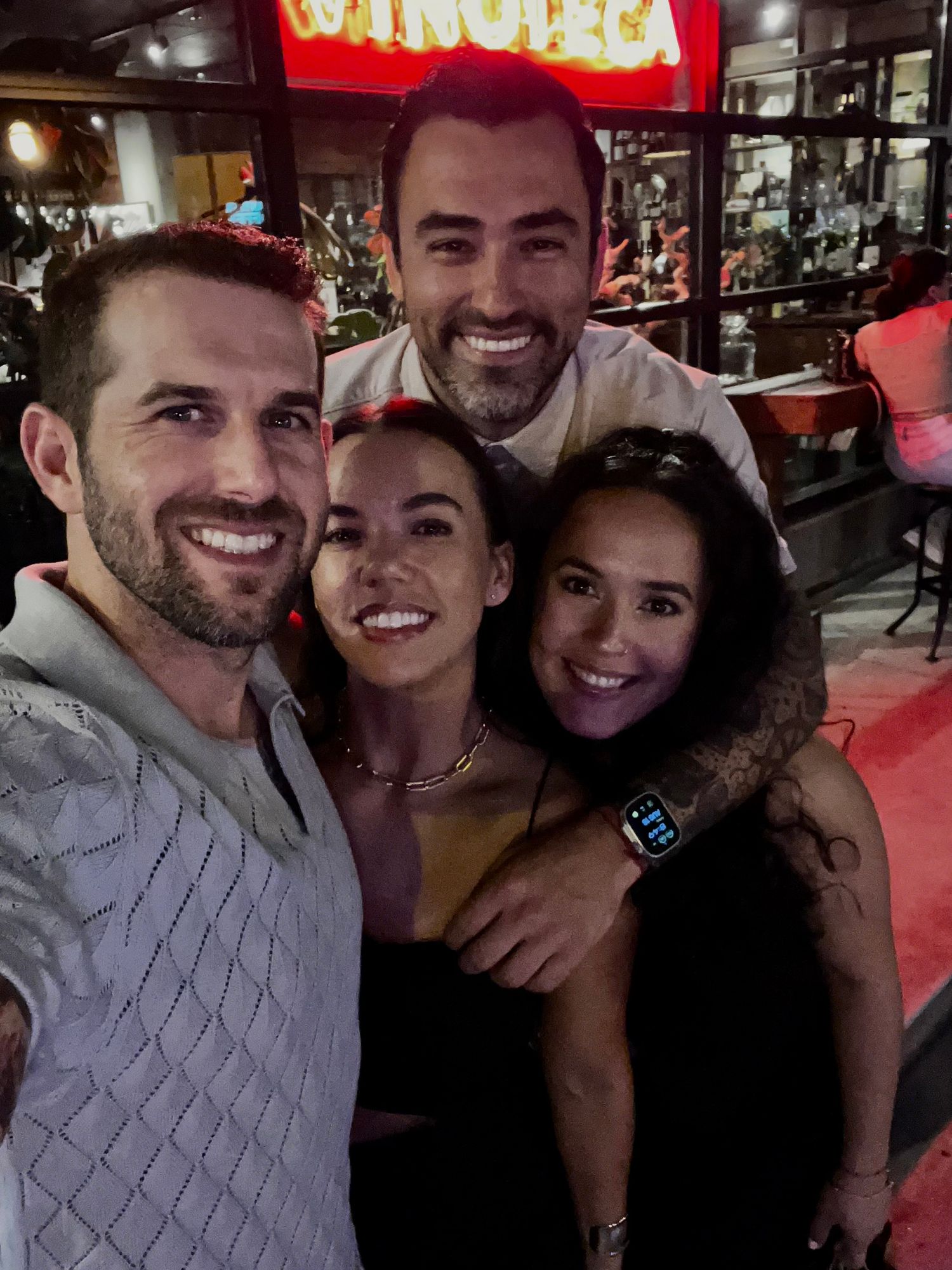 Group of four friends smiling together for a selfie outside a restaurant at night.
