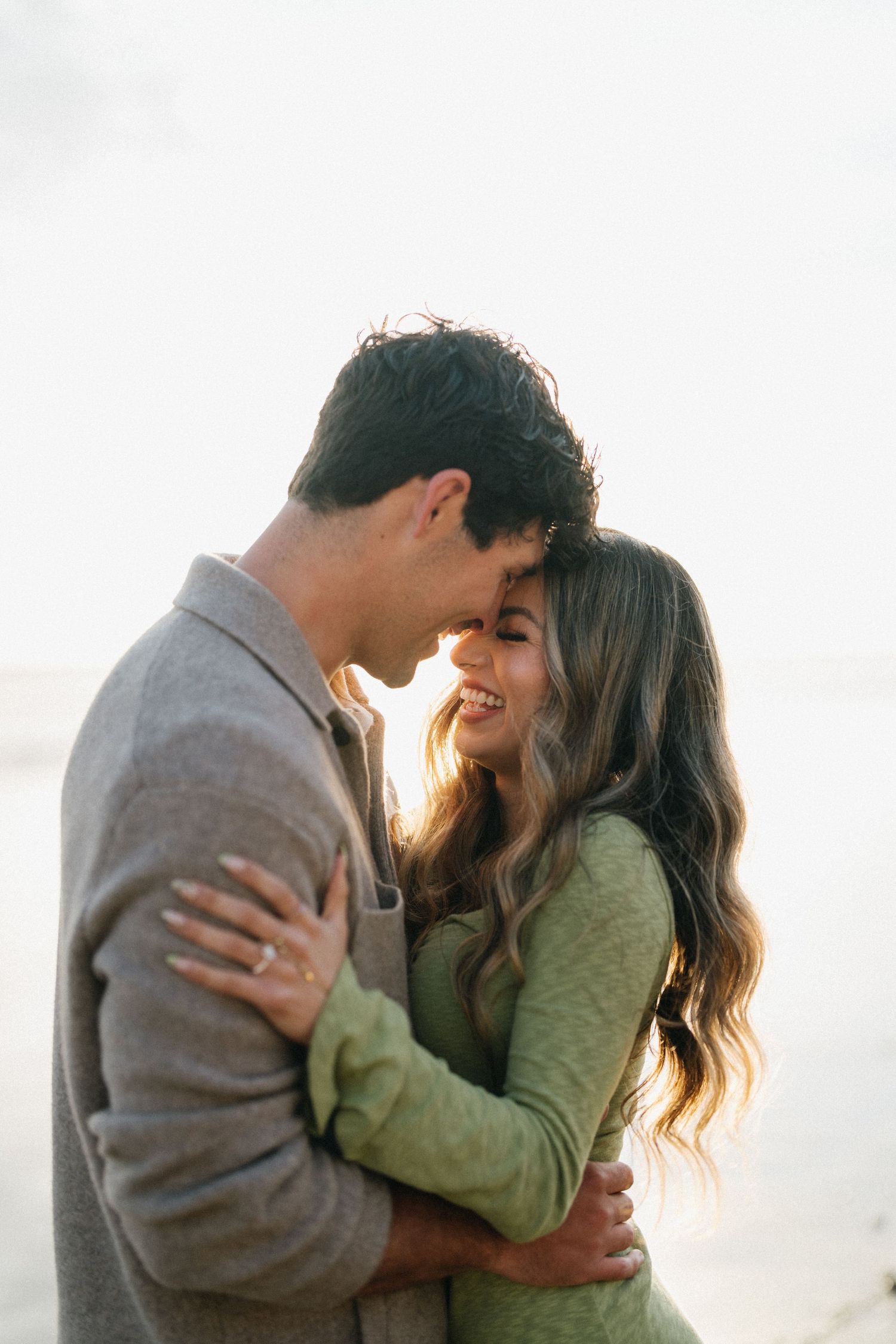 Smiling couple embracing warmly on a bright beach, woman wearing an engagement ring.