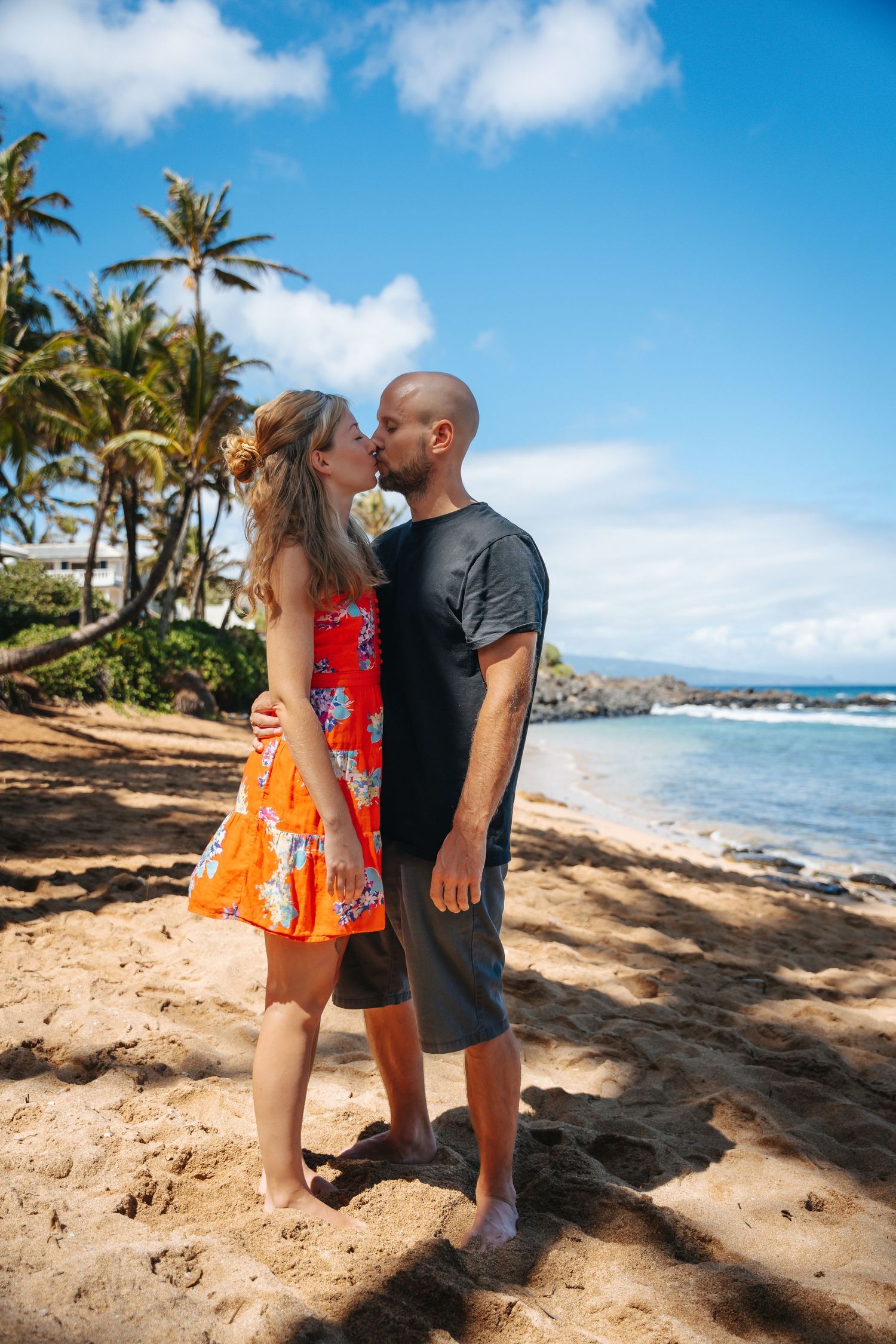Couple embracing on sandy beach with palm trees and ocean views in Hawaii.