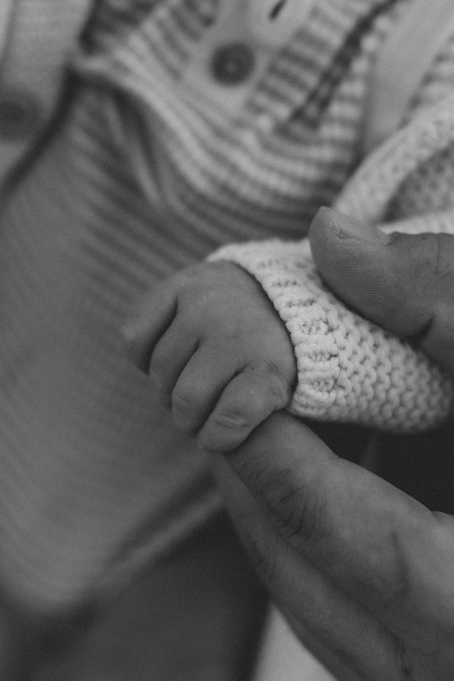 Close-up black and white image of tiny baby fingers grasping dads hand.
