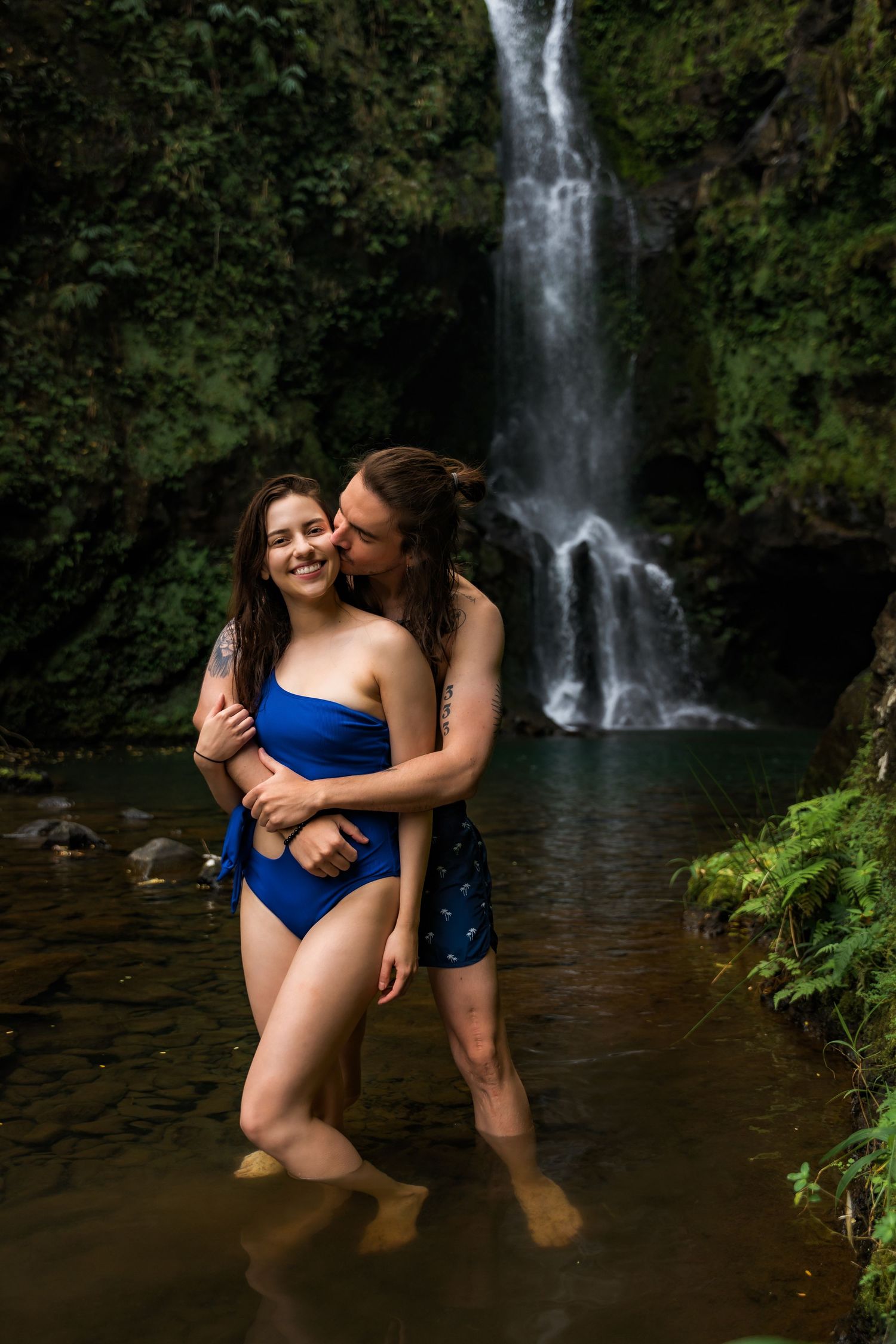 Intimate photoshoot at a tropical waterfall with two people in blue swimwear.